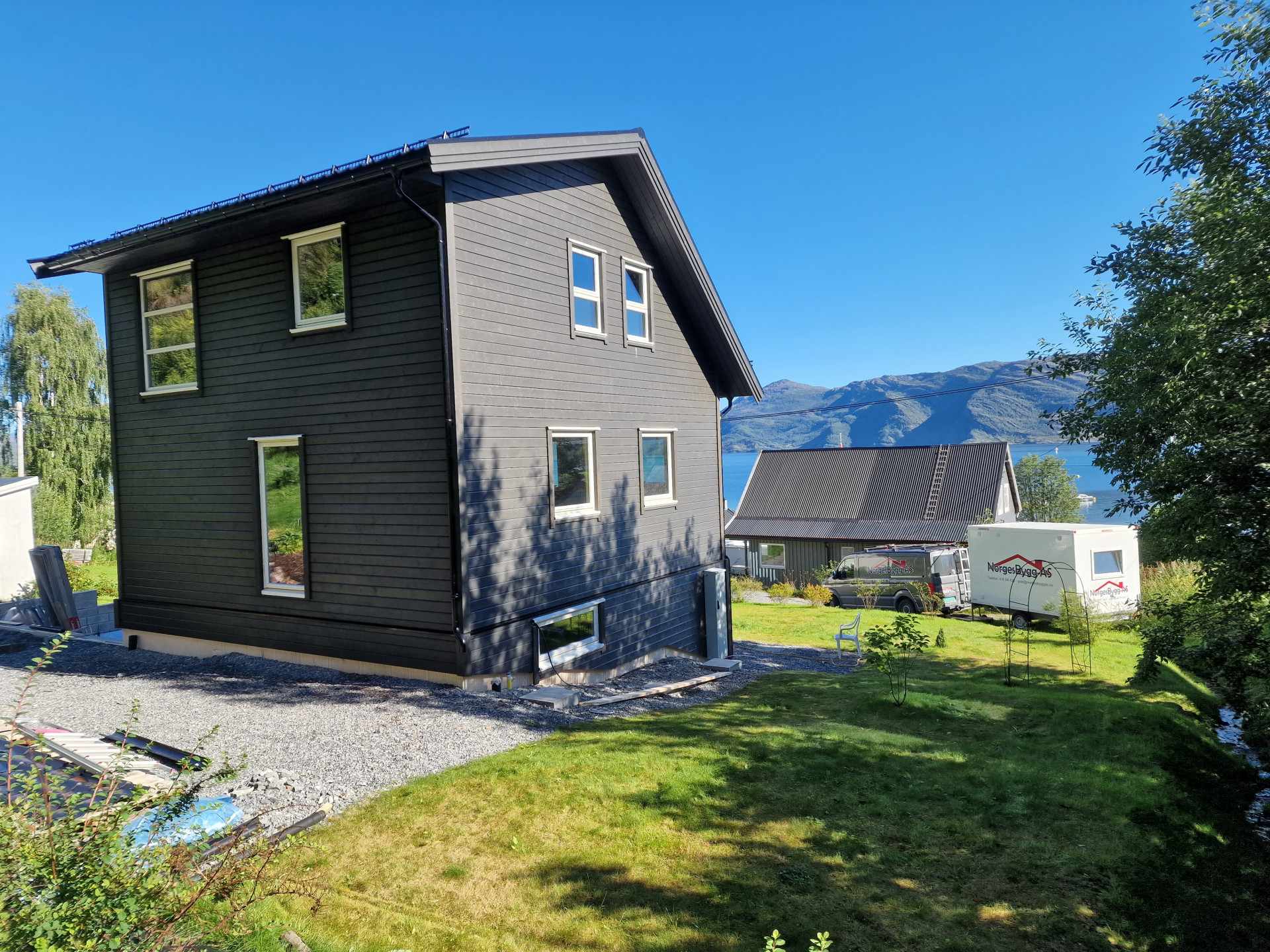 Ferdigstilt enebolig med mørk trekledning ved fjorden, bygget av NorgesBygg AS
